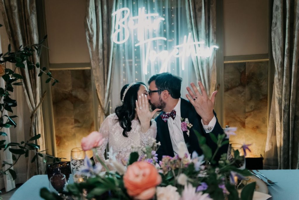 bride and groom kissing in front of neon sign 