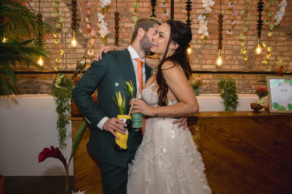 Bride and Groom in front of bar with Tiki Drinks and Hanging Lights